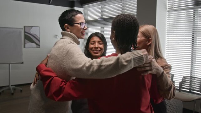 Dynamic zoom in shot of multiethnic group of smiling women embracing in circle ending successful support group meeting and healing together