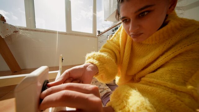 Focused Female Worker In Yellow Garment Tightens Caster Wheel Under Table With Screwdriver During Daylight