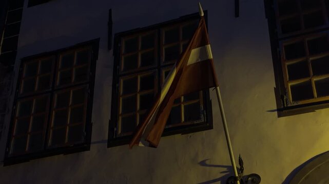 Historic building illuminated at night. Flag waving on pole beneath illuminated windows in city at night