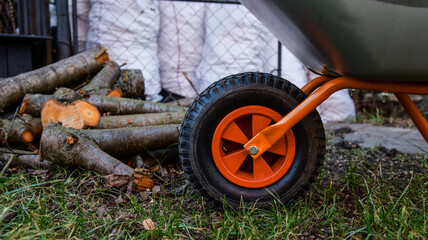 Gardening wheelbarrow with pile of logs and white bags in the background