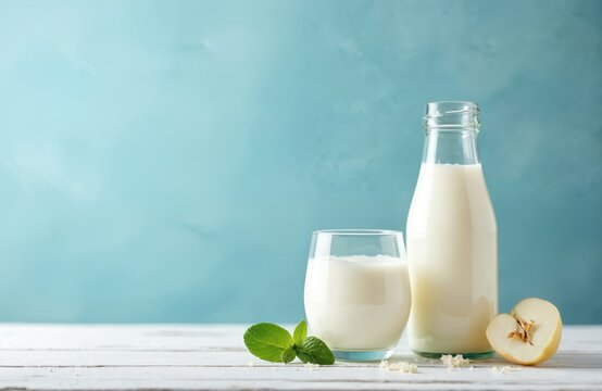 Glass and bottle of kefir or yogurt drink on white wood table. Fresh mint and quince slice next to beverage. Blue wall background and copy space.