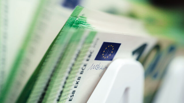 Money counting machine processing stacks of cash with visible Euro banknotes, showcasing detailed currency features and a clean, organized workspace environment