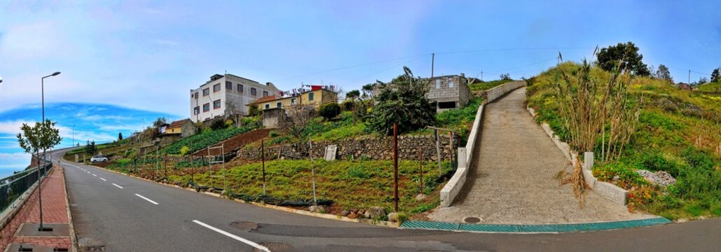 Coastal Village Serenity: A panoramic view captures a charming coastal village nestled on a hillside, with quaint houses, winding paths, and lush greenery meeting the vibrant blue sky.