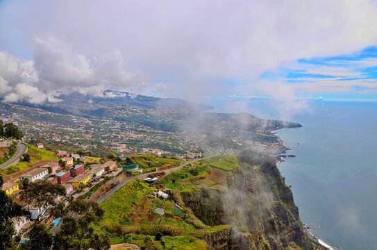 A dramatic high-angle view of misty Portuguese coastal cliffs overlooking a sprawling town and sparkling ocean.