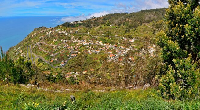 A breathtaking panoramic view of a hillside town in Madeira, Portugal, nestled in green landscapes overlooking the sparkling Atlantic Ocean.