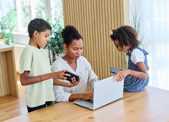 Obraz premium Portrait of ayoung businesswoman working on laptop from home distracted by surrounding noisy children. Motherhood, childhood, family, freelance job, home office concept
