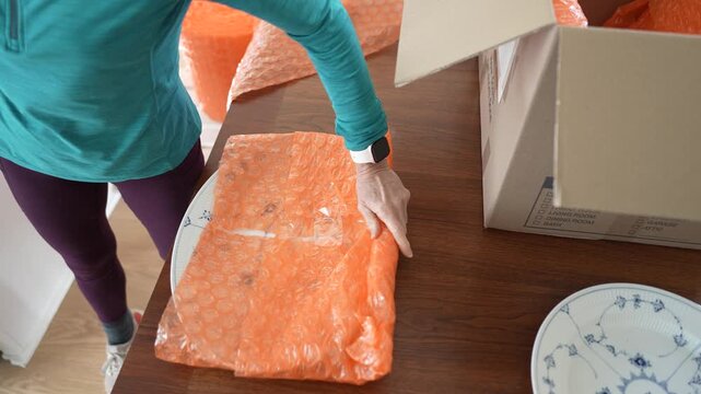 Mature woman wraps family heirloom china with care before placing it in a box for shipping to a family member in her home