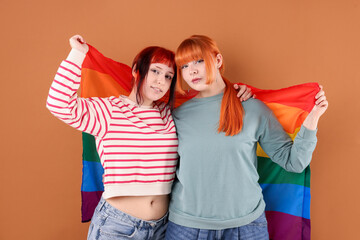 Lovely lesbian couple with rainbow flag on brown background. LGBT concept