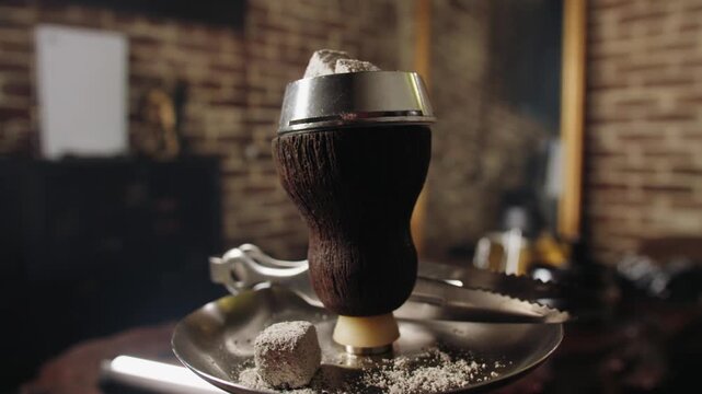 Closeup of wooden hookah bowl on metal tray with tongs and foiltopped head with coking glowing coals. Cozy lounge vibe in hookah bar with brick wall background. Preparing for vacation. No people