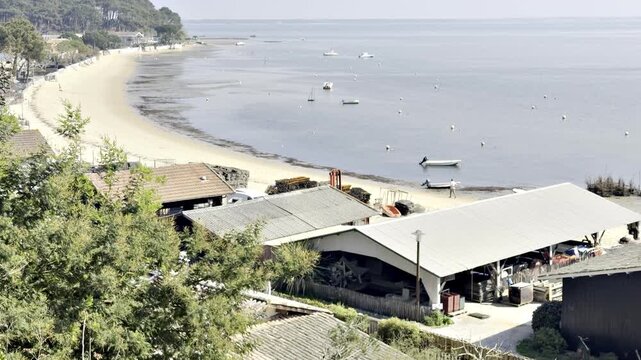 Wide shot of oyster farming buildings at Cap Ferret with a scenic beach facing Arcachon Basin, illustrating traditional shellfish industry in a coastal landscape of southwest France