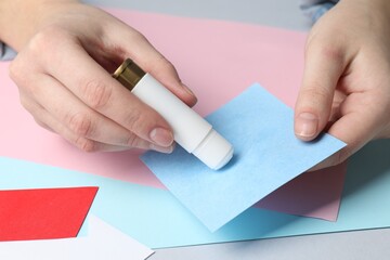 Obraz premium Woman applying glue onto paper at light grey table, closeup