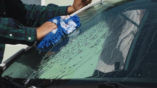 Man wiping the windshield of a car with a cloth, showing vehicle cleaning, maintenance, and outdoor care routine.
