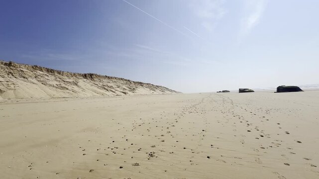 Expansive view of Cap Ferret point beach with German World War II blockhouses isolated on the sand while the dune face gradually collapses onto the shoreline under ongoing coastal erosion