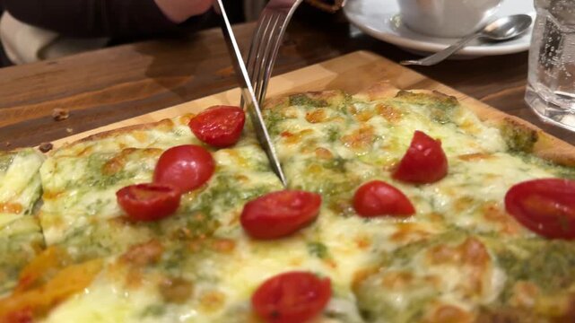 Pesto pizza BBQ chicken with cream and nutty home made pesto sauce. A girl takes a slice of pizza with pesto sauce. A rectangular pizza in Italy.