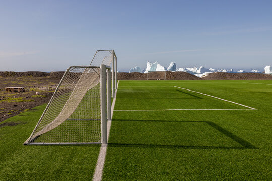 Soccer goal on green field with floating icebergs in the background on Disko Island in Greenland