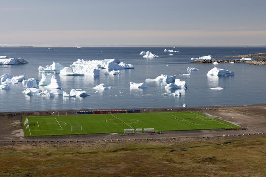 Elevated epic view of the arctic football field in Qeqertarsuaq in Greenland with floating icebergs in the background