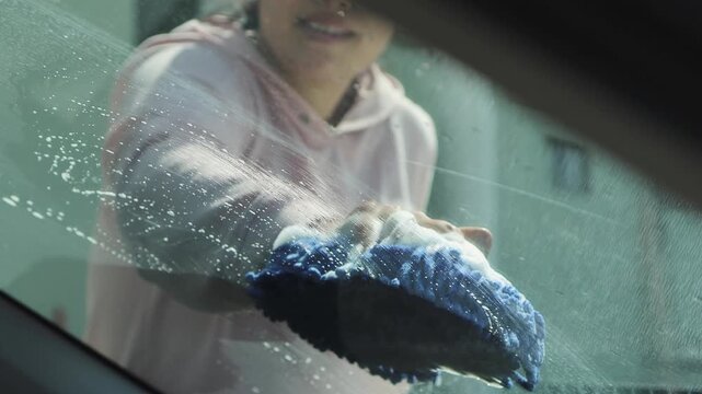 Woman wiping the windshield of a car with a cloth, showing vehicle cleaning, maintenance, and outdoor care routine.