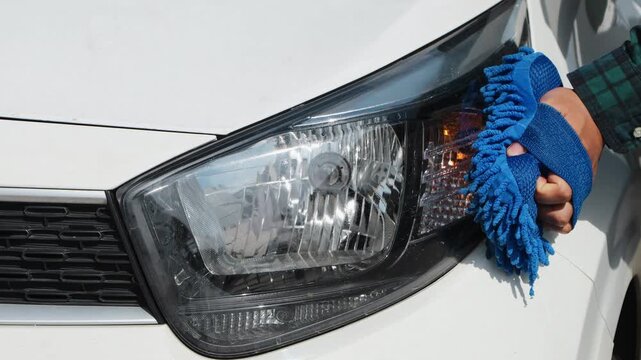 Close up of hands cleaning car headlights using a cloth, showing vehicle care, maintenance, and outdoor washing routine.