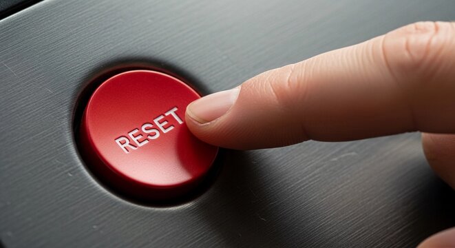 Finger about to press a red reset button on a dark surface