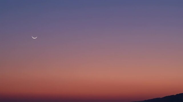 A crescent moon in a twilight sky with a gradient of purple to orange