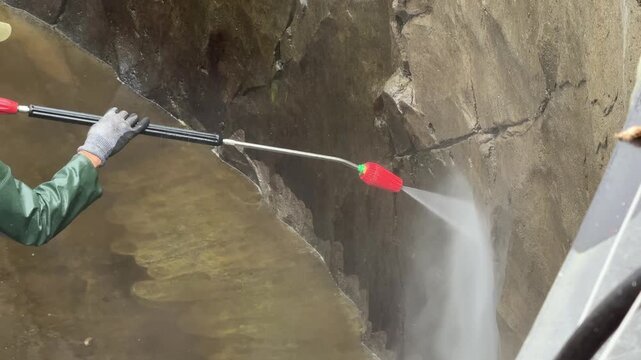 Worker cleaning stone wall with pressure washer removing dirt and algae in outdoor maintenance work