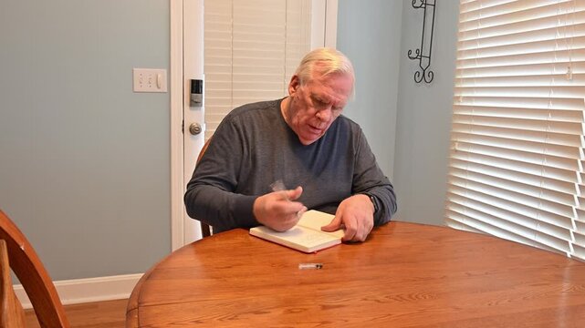 Man sits at wooden table and opens a notebook. He writes, focused, with a pen. His expression shows quiet concentration. Ideal for scenes of personal reflection or daily tasks