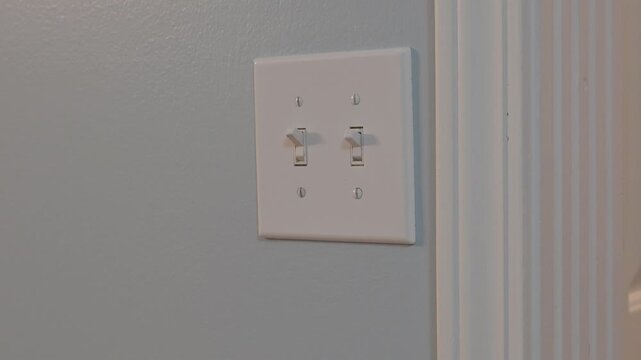 Hand in red sleeve faces a light switch. Palm open, ready to press. Light blue wall background. Hand pauses before action. Shows anticipation for turning on light. Ideal for home or routine scenes