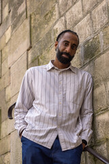 Obraz premium Portrait d'un bel homme souriant, noir d'origine antillaise, barbu. Il est adossé à un mur.