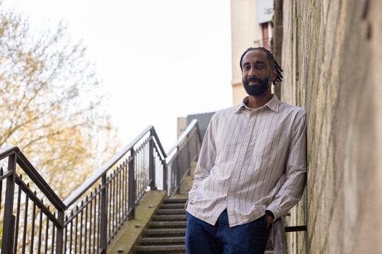 Un homme se tient sur un escalier ext&eacute;rieur en pierre, dans un cadre urbain structur&eacute; m&ecirc;lant architecture et nature.