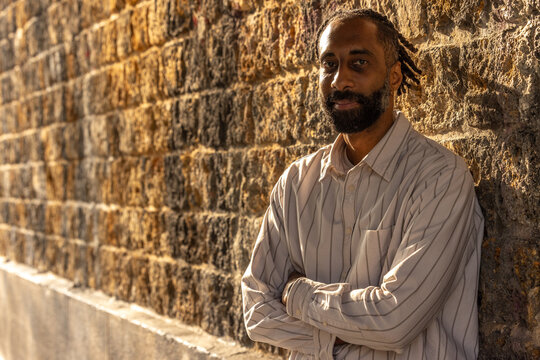 Portrait d'un bel homme souriant, noir d'origine antillaise, barbu. Il est adoss&eacute; &agrave; un mur.