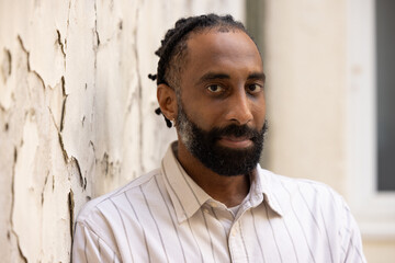 Portrait d'un bel homme souriant, noir d'origine antillaise, barbu. Il est adossé à un mur.