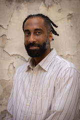 Portrait d'un bel homme souriant, noir d'origine antillaise, barbu. Il est adossé à un mur.