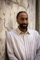 Portrait d'un bel homme souriant, noir d'origine antillaise, barbu. Il est adossé à un mur.