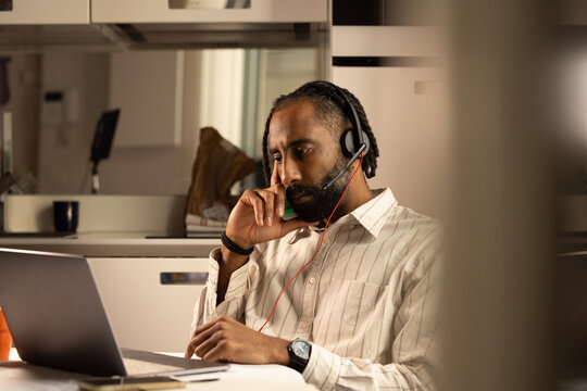 Portrait d'un jeune homme noir de 30 ans qui travaille &agrave; la maison en t&eacute;l&eacute;travail. Il est assis devant un ordinateur portable et il a un casque audio sur les oreilles