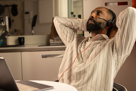 Portrait d'un jeune homme noir de 30 ans qui travaille &agrave; la maison en t&eacute;l&eacute;travail. Il est assis devant un ordinateur portable et il a un casque audio sur les oreilles