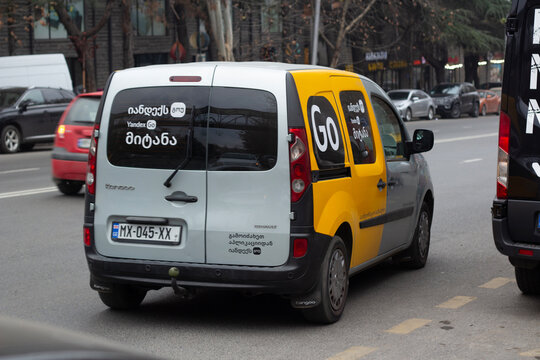 Tbilisi, Georgia - December 8, 2024: Horizontal street photo. Back view. Car with Yandex Go logo, yellow door. Concept of delivering healthy food. Translation from Georgian: Yandex Go, delivery