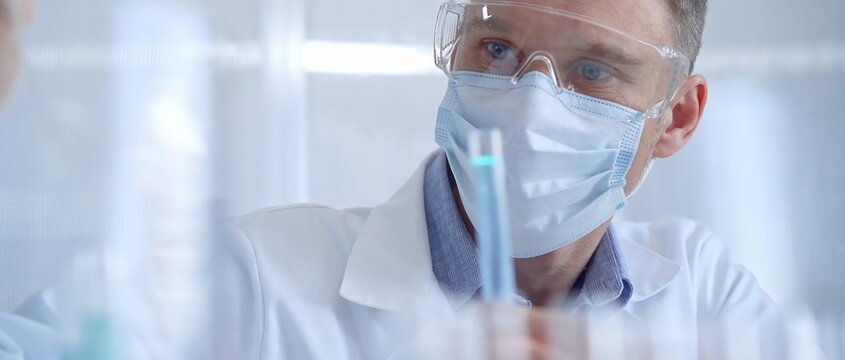 Man with safety glasses and blue mask is working with lab tubes using a pipette in a modern laboratory, close-up of researcher. Science and medicine