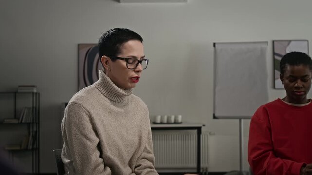 Tilt up shot of mature Caucasian woman crying in support group meeting and wiping eyes with tissue while speaking emotionally and sharing life story sitting on chair in circle, copy space