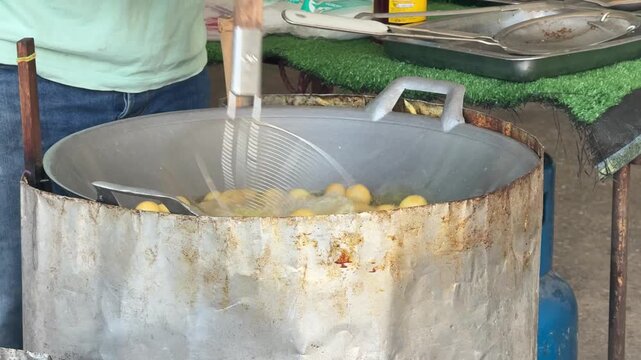 Traditional Thai sweet potato balls (Khanom Khai Nok Krata) deep-frying in a large wok.
