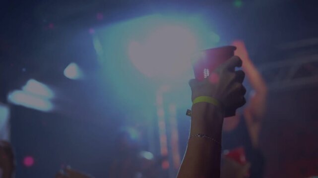 Music beat driving fan raising red cup wearing yellow band while singer singing and lights pulsing