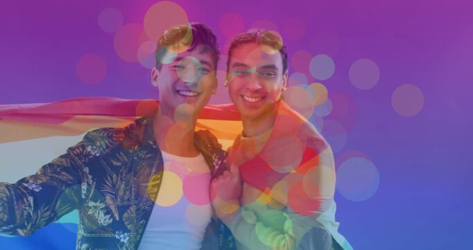 Vertical video: Couple leaning on set with bokeh rising wrapping pride flag jacket-clad for pride