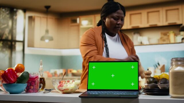 Mockup screen on laptop with african american woman doing meal prep on camera, showing the cooking process of a homemade dish. Creating culinary content for online audience.