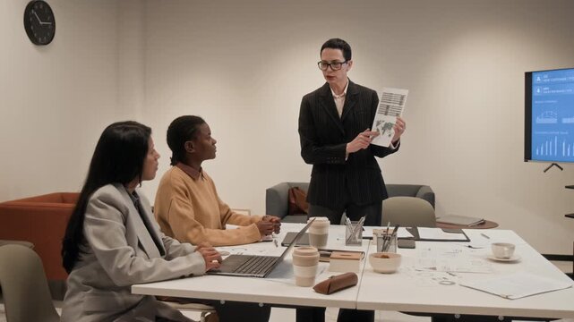 Front view shot of adult Caucasian woman as confident female boss pointing at charts while presenting data to team during business meeting in office, copy space