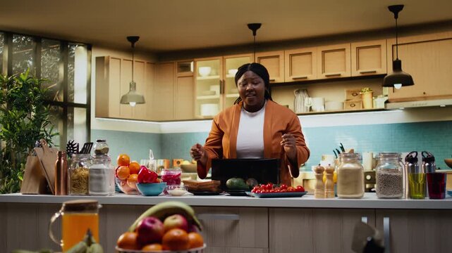 African American food influencer preparing avocado and toast with a toaster, meal prep at counter indoors. Woman vlogger filming culinary recipe and tutorial, healthy food breakfast idea.