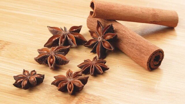 Macro rotating star anise and cinnamon sticks on a wooden board. Clean organic spice duo for culinary, baking, and traditional medicine.