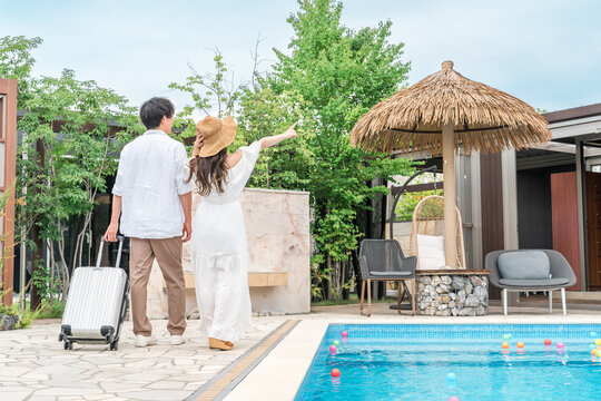 A young Asian couple walking by the poolside of a resort hotel (traveling, honeymoon, vacation)