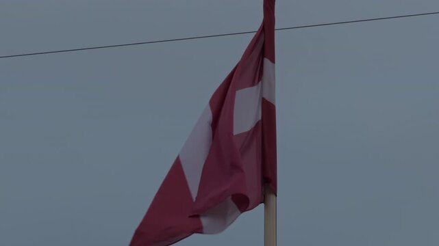 Flag sways in breeze. Latvian banner rippling high. Deep red and white Latvian flag waves calmly in gray sky