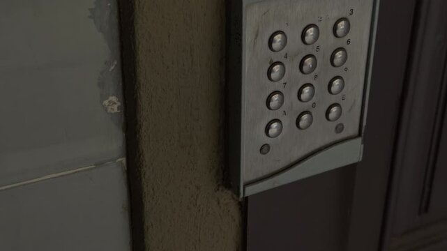 Aged door keypad. Rusty keypad with scratched numbers and chipped paint at shadowed urban apartment entrance