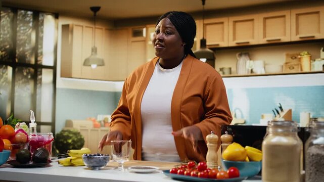 African American food vlogger preparing nutritious chia seeds yogurt bowl in home kitchen. Content creator filming cooking process and adding ingredients to create protein rich breakfast idea.
