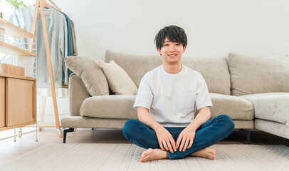 Fototapeta premium A smiling young Asian man sitting in front of the sofa in the living room.